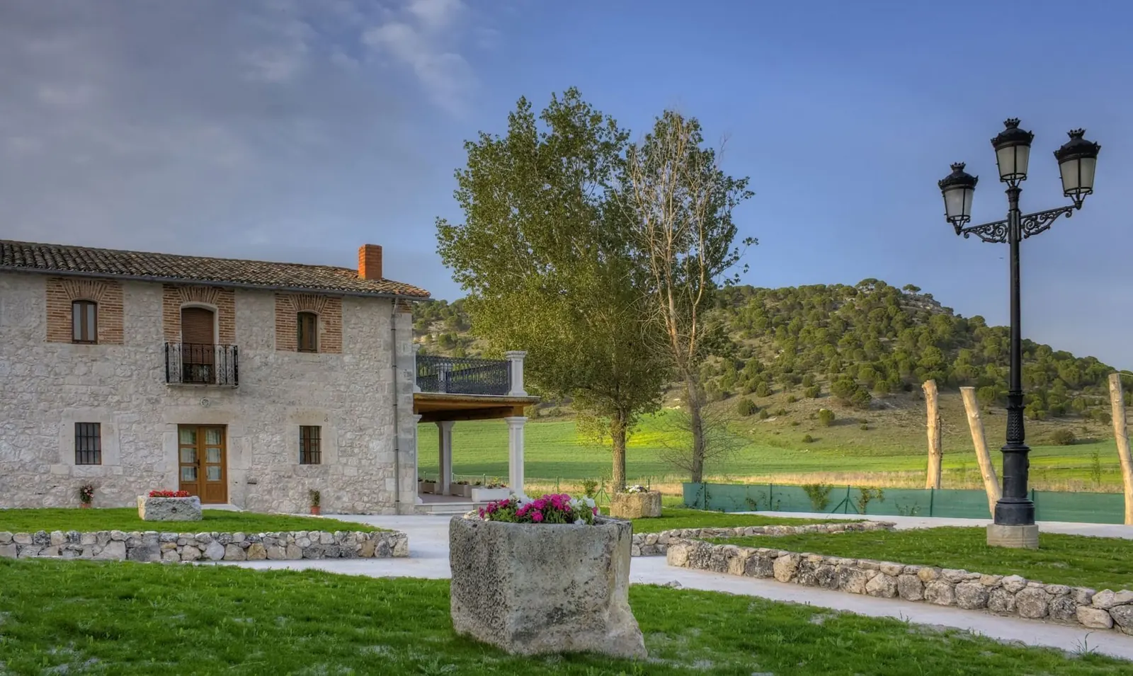 Caserío de piedra de Casa Valimón con jardines y estanque, rodeado de campo castellano
